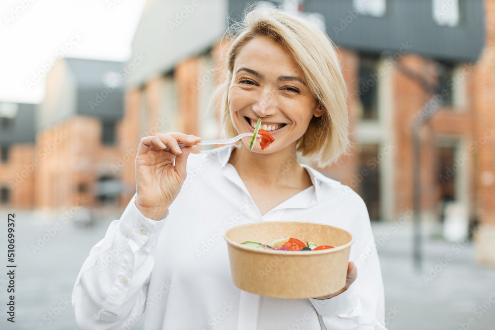 Portrait of smiling business woman eating healthy salad while having break during work. Kind positiv female eating her salad while being on the city street. Portrait of smiling business woman eating healthy salad while having break during work. Kind positiv female eating her salad while being on the city street.