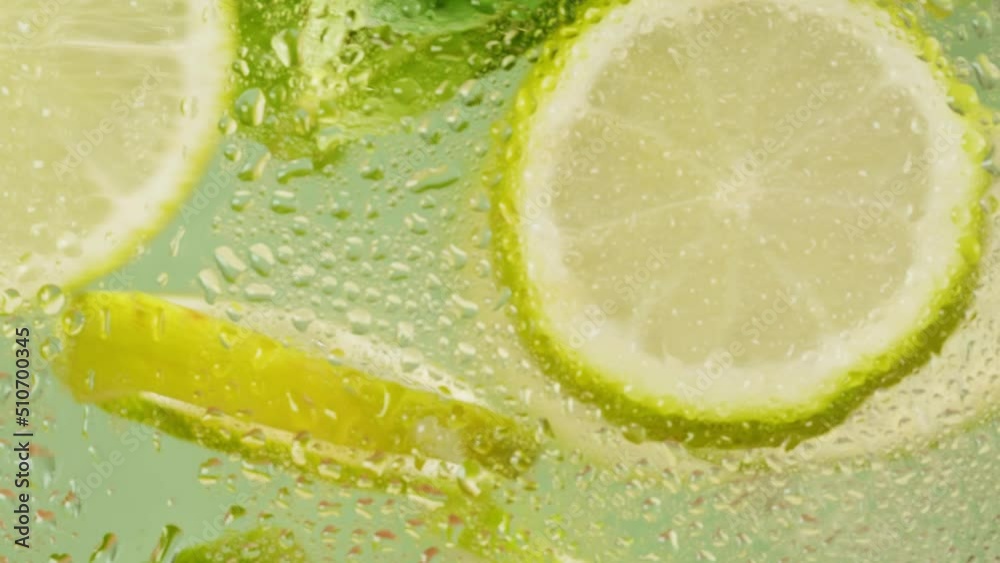 Lemon and lime cocktail, cooking cold lemonade, citrus fruits in water on green background, shooting of carbonated water with floating sliced fruits. 