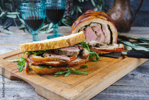 Traditional barbecue Italian porchetta pork belly roll meat sandwich with rocket salad served as close-up on a rustic wooden board