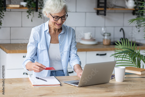 Beautiful senior woman with short grey hair and lovely smile shopping in the internet at home with a credit card. Concept of mature woman using technology