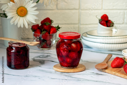 Homemade strawberry jam in glass jars with fresh strawberry on wooden boarding. Kitchen table decorated chamomiles with fresh strawberry jam, morning breakfast concept. photo