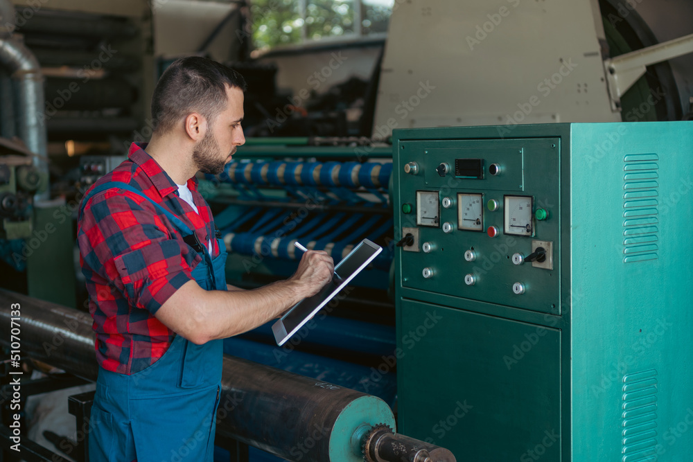 The employe at the work, writing down some digits, which he is reading of the machine