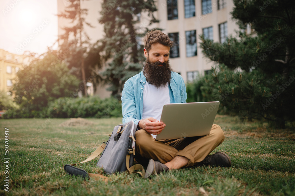 Beard man entrepreneur sitting outside, working on his laptop. He is relaxed, smiling and enjoying his time outside. Beard man entrepreneur sitting outside, working on his laptop. He is relaxed, smiling and enjoying his time outside.