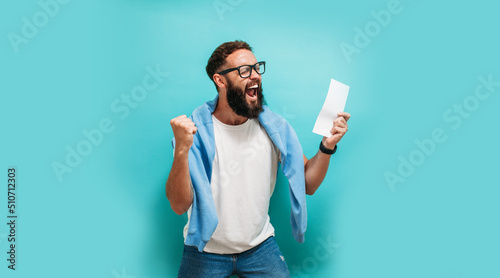Excited happy young male winner feeling joy winning lottery, placing bets, getting cashback online gift isolated on blue background. Human face emotions and betting concept. Trendy colors