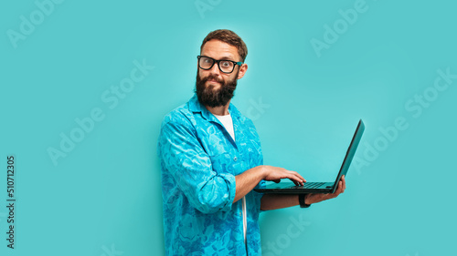 Young crazy bearded charismatic man. Shocked or surprised expression. Laptop concept. Funny promotion poster. Programmer, web developer holding a laptop in his hands and looking at the camera photo