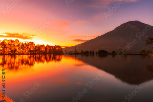 Sunrise with Mount Sumbing with lake surface on the foreground. The lake surface make reflection of mountain and sunrise sky. Embung Kledung, Central Java, Indonesia 