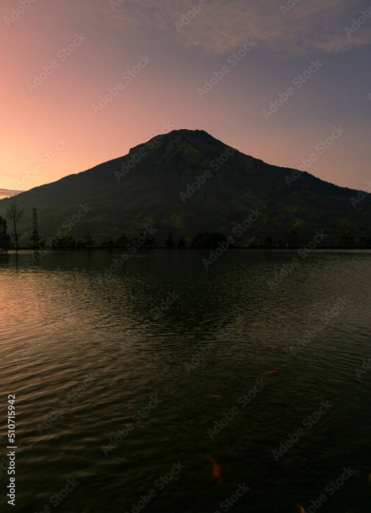 Sunrise with Mount Sumbing with lake surface on the foreground. The lake surface make reflection of mountain and sunrise sky. Embung Kledung, Central Java, Indonesia
