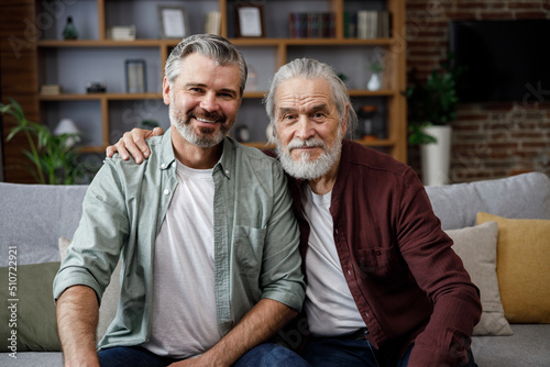Obraz na plátně Handsome smiling adult man hugging senior mature father, looking at camera