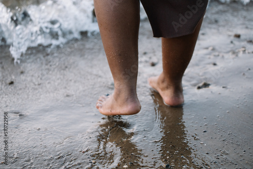 Closeup unrecognizable dark skin barefoot woman legs walking through seaside, beach, foam wash. Interracial female on vacation. Mixed race people, ethnicity, diversity. Multicultural person in summer