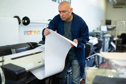 Man working in publishing facility  loading large format paper in printer.