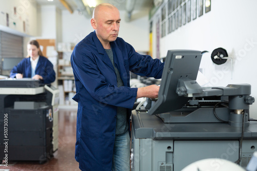 Man working in publishing facility  using printer  pushing buttons on display.