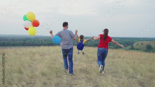 happy family. dad mom child run across field with colorful balloons. happy family concept. kid child running with mother father for walk. parents play with little girl daughter. childhood dream fly.
