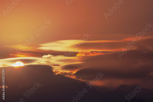 The sun rises among the clouds above the silhouettes of mountain hills. © Franchesko Mirroni