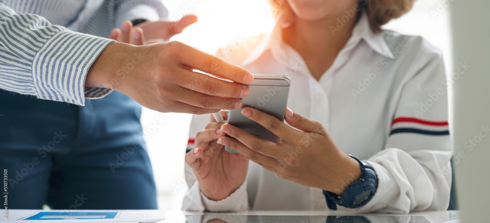 Two young businesspeople talking and discussing together at office, using smartphone analyzing  marketing and planning business.