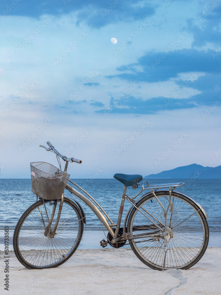 Fototapeta premium The bike is on the sandy beach. Against the background of the blue sky with the moon