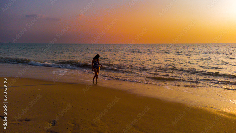 Happy Carefree Woman Enjoying holiday. Woman silhouette walking on the beach at sunset. 