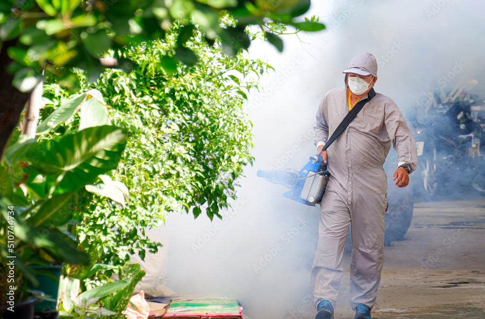 Outdoor healthcare worker using fogging machine spraying chemical to eliminate mosquitoes and prevent dengue fever on overgrown at slum area