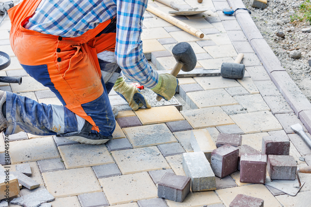 A squatting worker lays paving slabs with a rubber mallet. A squatting worker lays paving slabs with a rubber mallet.