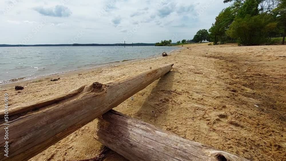 Deserted beachfront at the at Ebenezer Church Day-Use Area of Jordan Lake State Recreation Area. Dramatic clouds and driftwood in the foreground. Clean sand, no trash. Gentle waves lapping the shore. Deserted beachfront at the at Ebenezer Church Day-Use Area of Jordan Lake State Recreation Area. Dramatic clouds and driftwood in the foreground. Clean sand, no trash. Gentle waves lapping the shore.