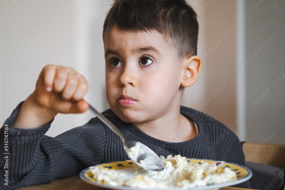 Boy eating breakfast cereals in bowl sitting by table look aside. Healthy diet lifestyle concept. Healthy breakfast. Healthy meal. Boy eating breakfast cereals in bowl sitting by table look aside. Healthy diet lifestyle concept. Healthy breakfast. Healthy meal.