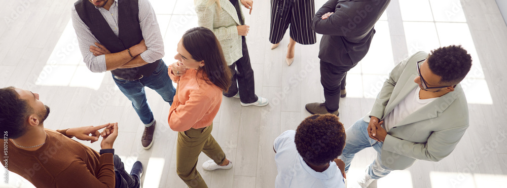 Young people meeting, interacting and making contacts at business event session. Group of multi ethnic participants standing in office and talking. High angle, overhead top view, above. Header, banner - obrazy, fototapety, plakaty 