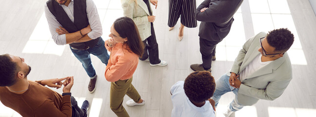 Young people meeting, interacting and making contacts at business event session. Group of multi ethnic participants standing in office and talking. High angle, overhead top view, above. Header, banner