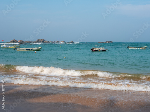 Hikkaduwa, Sri Lanka - March 4, 2022: Beautiful view of the beach in Hikkaduwa. People swim in the Indian Ocean near the boats. Copy space