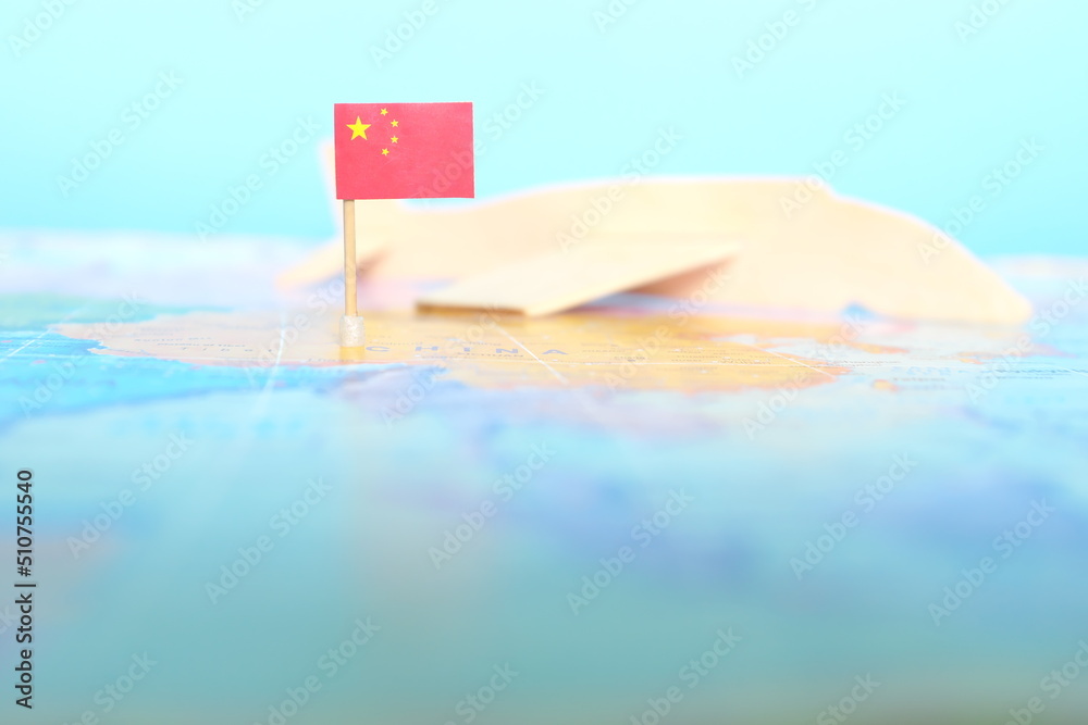 Selective focus of Chinese flag in blurry world map and wooden airplane model. China as travel and tourism destination concept.	