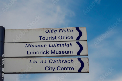 Sign in English and Irish language in Limerick city with direction to Tourist office  Museum and city centre. Blue cloudy sky background.