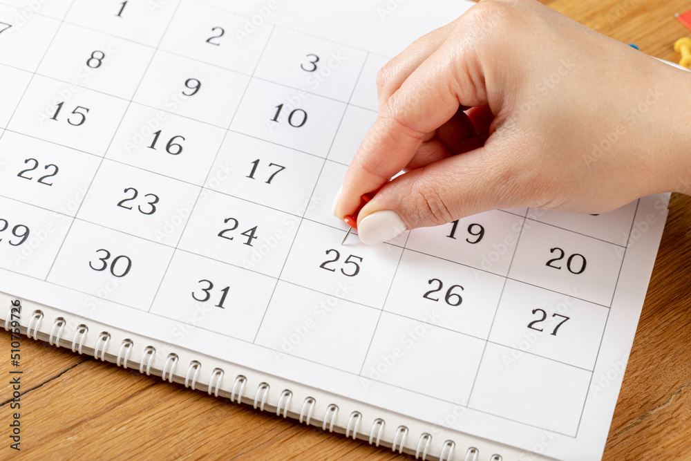 beautiful female Hand with manicure pushes a red pin on a calendar 25 day beautiful female Hand with manicure pushes a red pin on a calendar 25 day