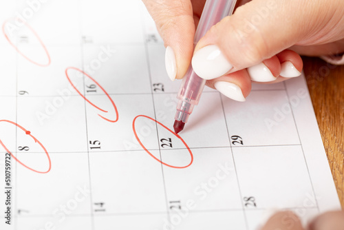 close up on employee woman hand using red pen to writing schedule on calendar 2022 to make an appointment meeting or manage timetable each day at house for work from home concept