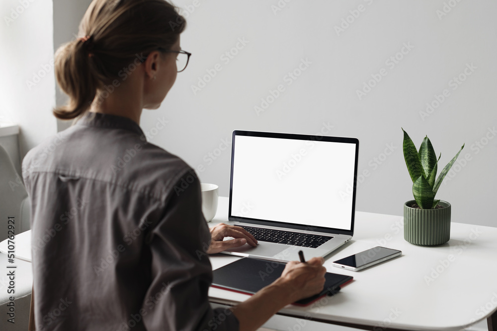 Young woman using laptop computer with white mockup screen at home. Business woman working in office. Freelance, student lifestyle, e-learning, web site, technology and online meeting concept - obrazy, fototapety, plakaty 