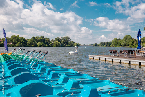 Colored Pedal boats at a wooden pier on a lake. Group of colorful pedal boats next to the wooden pier of Lake. Plastic white Swan Pedal Boat On Aasee (Aa-Lake) Muenster Germany. Active rest outdoor