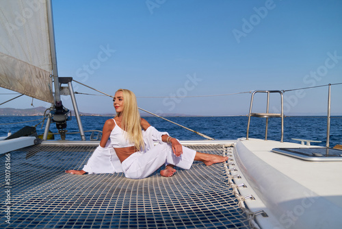 Beautiful young blond woman sitting on catamaran at sunny summer day