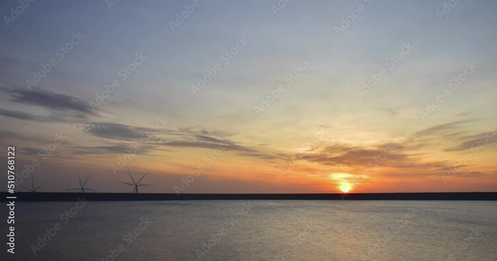 The sun rises over the water between the wind turbines in operation. The sun rises over the water between the wind turbines in operation.