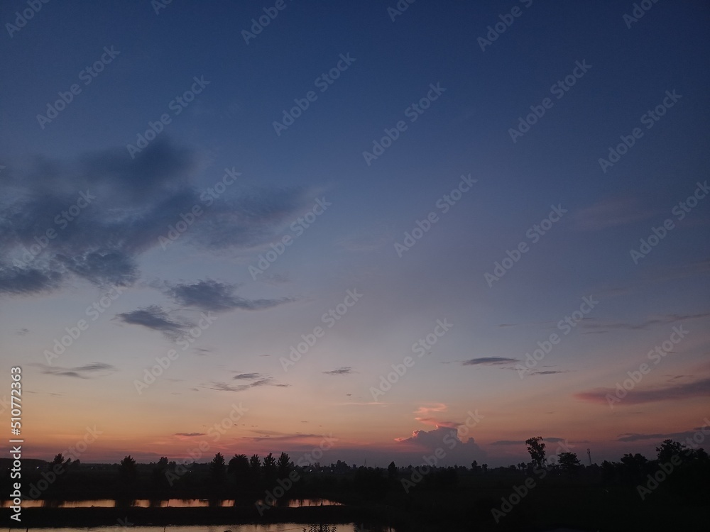 sunset in the village, blue sky, trees, clouds in the sky 