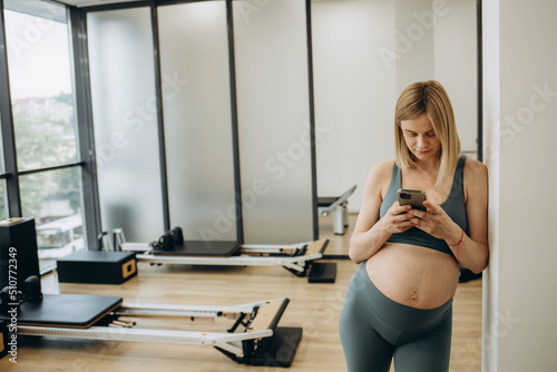 Young pregnant woman practicing yoga at home and using phone