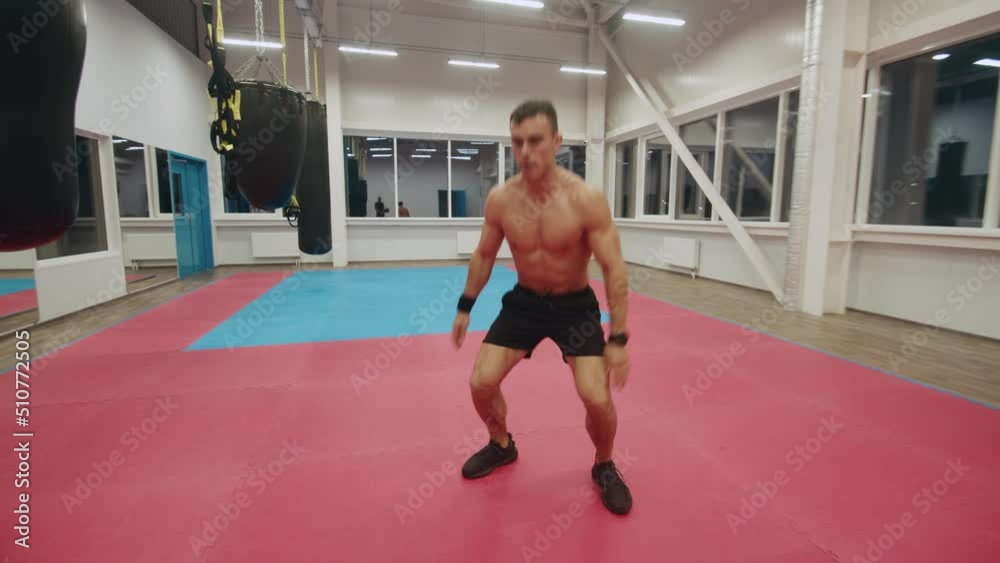 Muscular man in black shorts in the gym and performs jumps and leg raises. Bodyweight training Muscular man in black shorts in the gym and performs jumps and leg raises. Bodyweight training