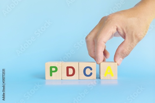 PDCA or Plan Do Check Act cycle method concept. Hand putting action wooden blocks in blue background with copy space.