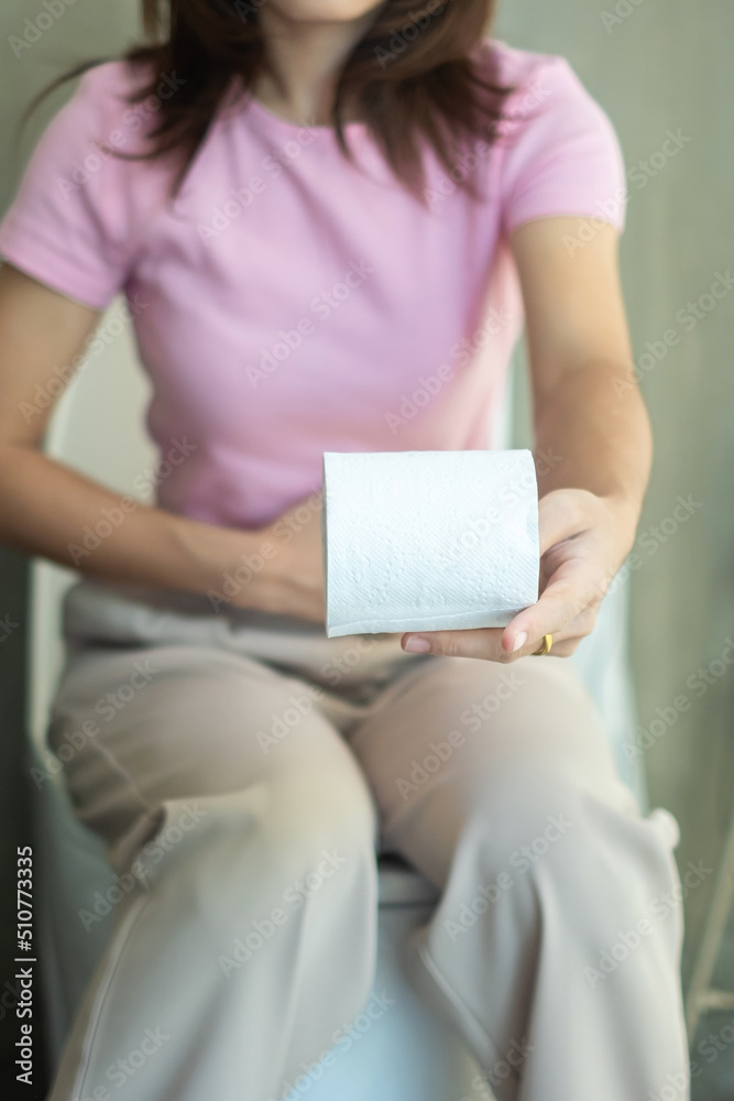 Woman holding toilet paper roll during sit on toilet bowl. diarrhea