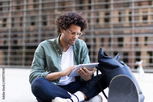 Young man with curly hair using digital tablet. Man sitting outside taking a break