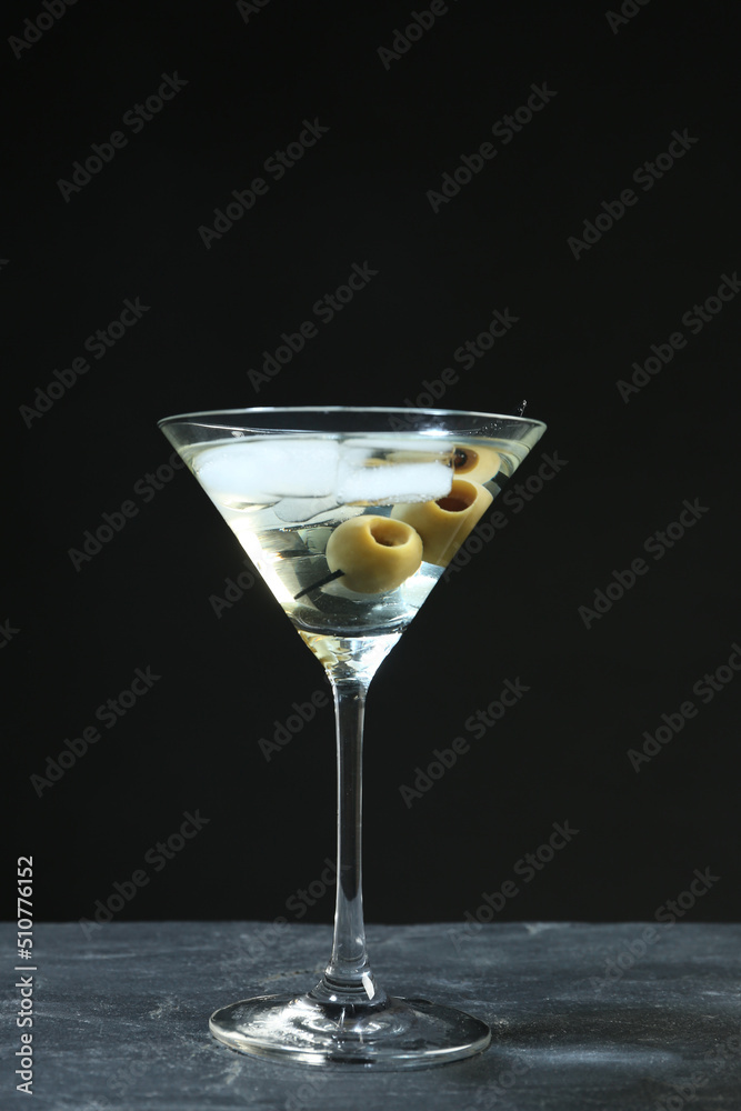 Martini cocktail with ice and olives on grey table against dark background