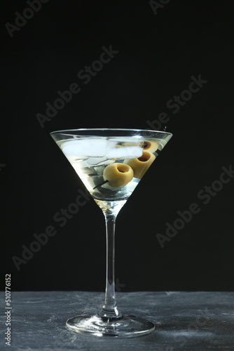 Martini cocktail with ice and olives on grey table against dark background
