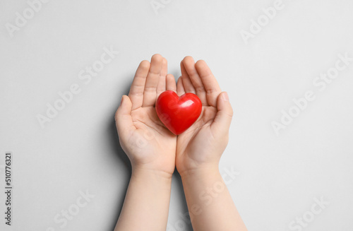 Child holding red heart on light grey background, top view