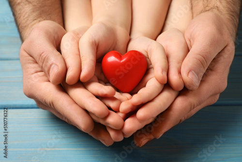 Parents and kid holding red heart in hands at light blue wooden table  closeup