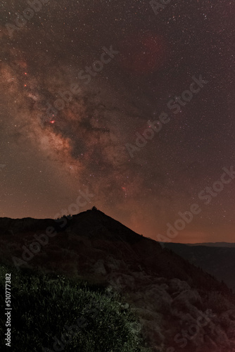 Milky Way above rugged mountain peak with illuminated brush in foreground
