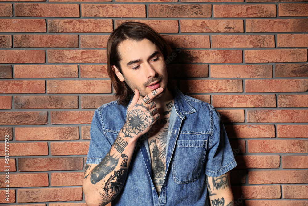 Young man with tattoos on body near brick wall Young man with tattoos on body near brick wall