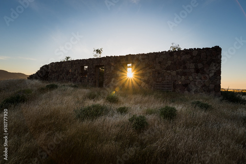Rocky building ruins surrounded by dry grass with sunstar at sunrise