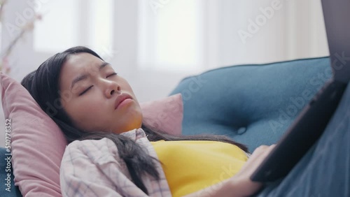 Young Asian woman falling asleep with laptop on sofa, overworked freelancer photo