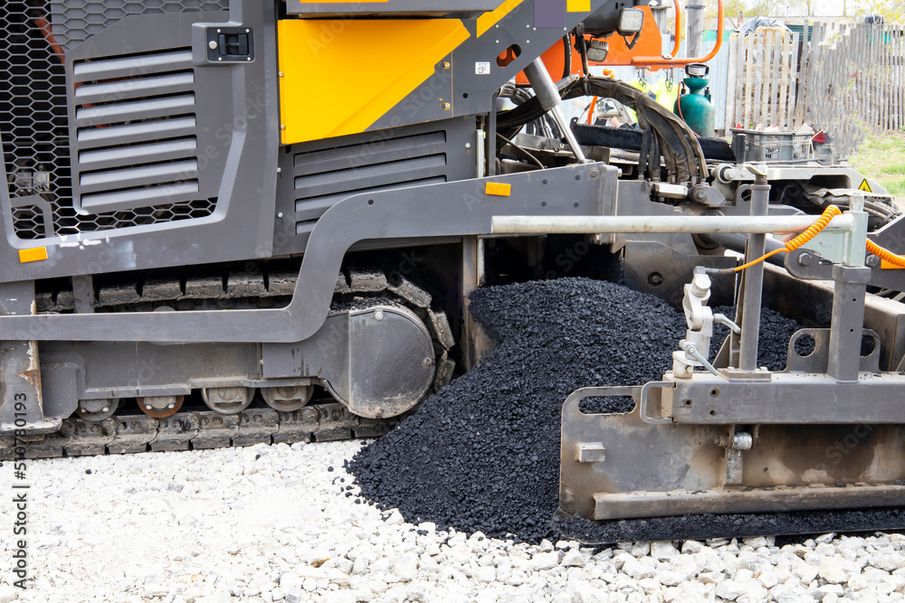 Worker operating asphalt paver machine during road construction and repairing works. A paver finisher, asphalt finisher or paving machine placing a layer of asphalt. Repaving